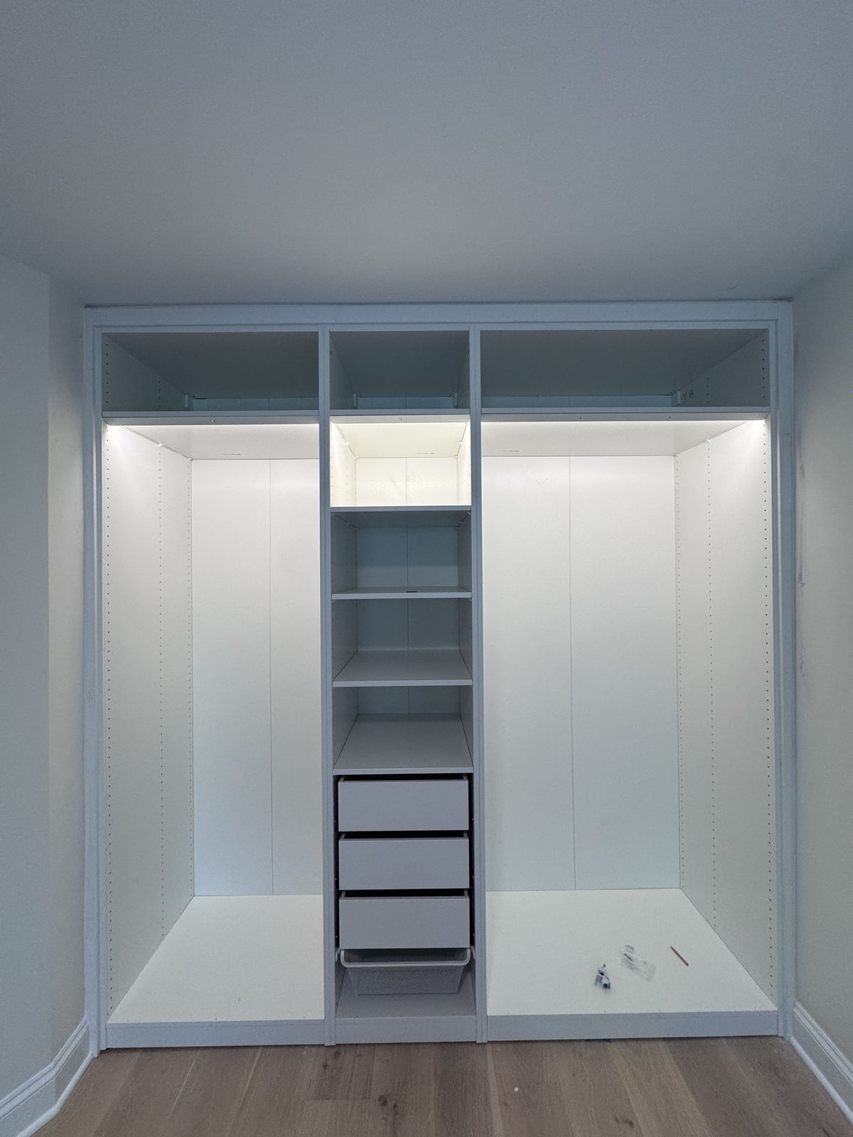 Real ModuCloset installation — illuminated closet interior with hanging storage, shelves and drawers.