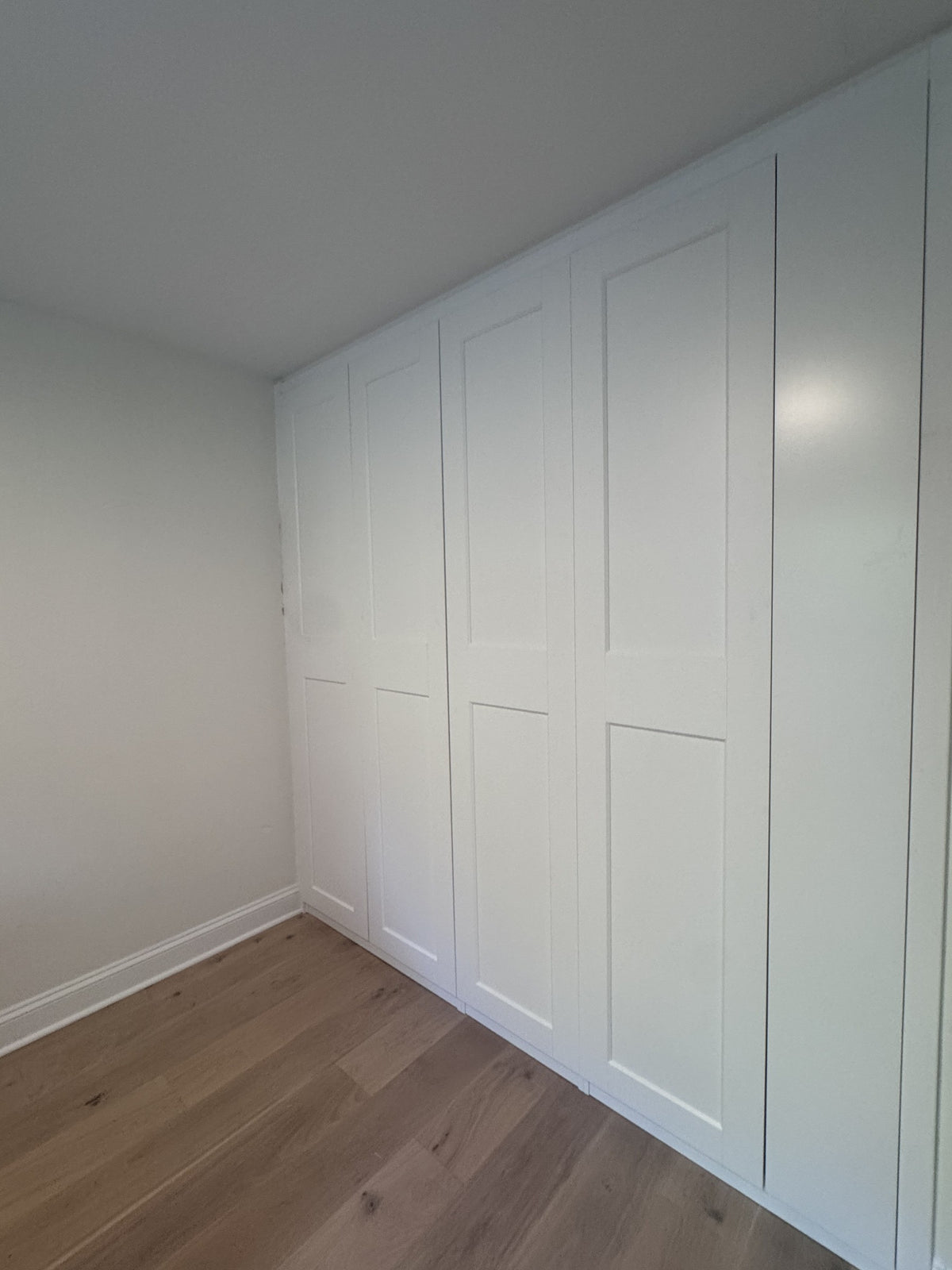 Real ModuCloset installation — finished white built-in closet with closed Shaker doors, angled view.