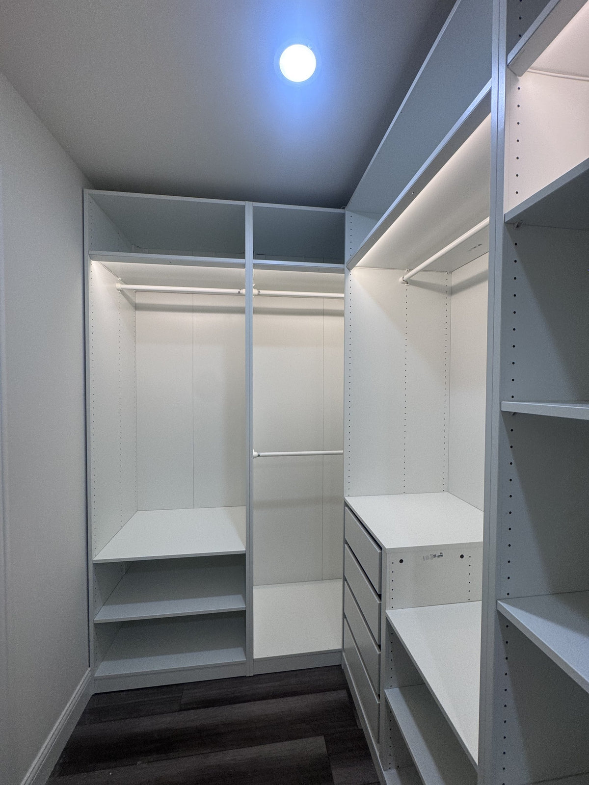 Real ModuCloset installation — walk-in closet view showing illuminated hanging storage and drawers.