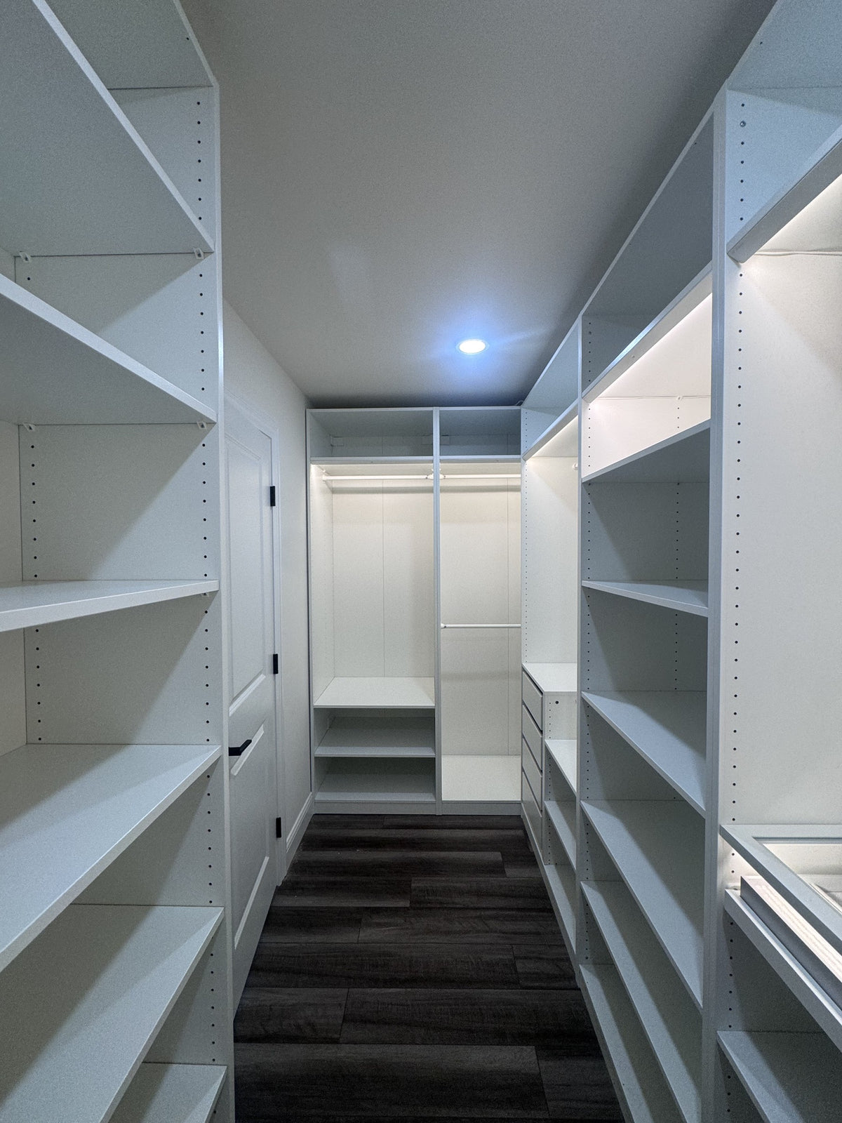 Real ModuCloset installation — full walk-in closet overview with illuminated hanging bays, shelves and drawers.